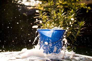 Spring Cleaning outside with big yellow cleaning gloves, water, soap and a big blue bucket with soap. Cleaning the table. Soap Foam on the table. Hands in bucket. Holding and wringing cleaning sponge. © Pepijn