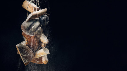 Fototapeta na wymiar white flour falling at loaves of bread, baguettes and croissant on ropes on black background with copy space