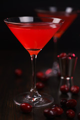 Cosmopolitan cocktail with cranberries and jigger. Dark wooden background, high resolution