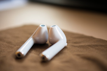 a pair of wireless, white earphones laying on a brown cloth, vintage-looking