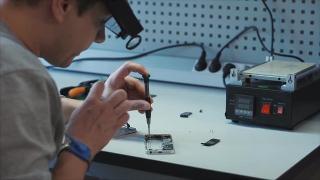 Closeup electronic expert identifies the cause of the breakdown of the gadget, uses a screwdriver and other special equipment. Employee uses special glasses