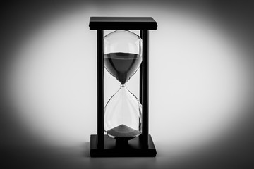 Black and white Hourglass with blue sand running through the glass bulbs ; time passing concept