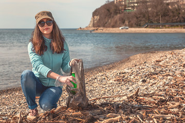A young woman puts the collected garbage in a bag and posing for the camera. Cleaning of the...