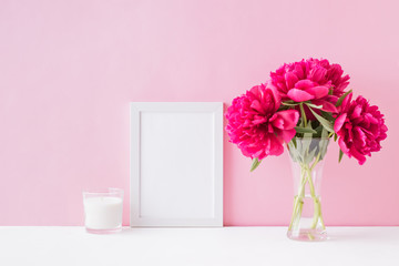 Mockup with a white frame and red peonies in a vase on a pink background