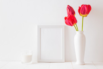 Mockup with a white frame and red tulips in a vase on a white wooden table