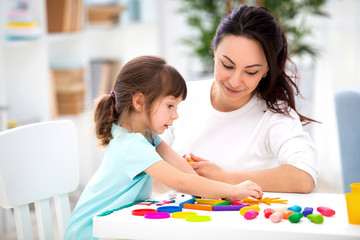 Smiling mother helps a little daughter to sculpt figurines from plasticine. Children's creativity. Happy family