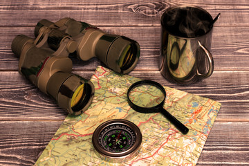 binoculars, magnifier, compass, mug, map on wooden background. travel, tourism.