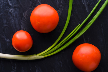 beautiful red tomatoes and green onions on black background