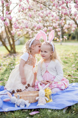 Little cute girls are sitting on the grass near the mogolia. Girls in costumes Easter bunnies.