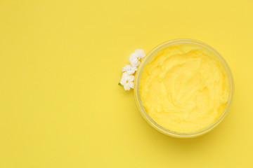 Container with natural scrub and white flowers on yellow background. Top view.Copy space.