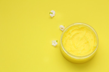 Container with natural scrub and white flowers on yellow background. Top view.Copy space.