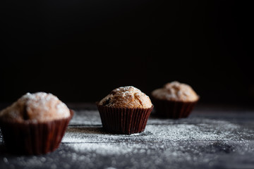 Three chocolate muffins on a wooden table a dark background. Place under the text
