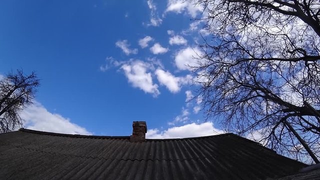 Time lapse of old brick chimney on a tiled roof against a cloudy sky at sunny day.