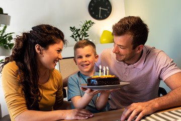 Happy family celebrating a birthday together at home. Young parents with son blowing candles on cake.