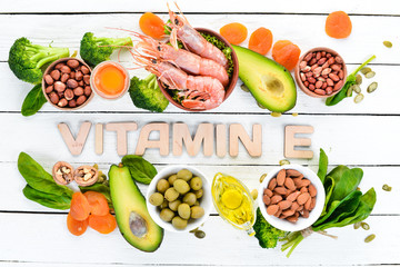 Food containing natural vitamin E: Spinach, parsley, shrimp, pumpkin seeds, eggs, avocados, broccoli. Top view. On a white wooden background.
