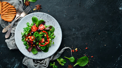 Vegetable salad with spinach, tomatoes, paprika and pumpkin seeds in a plate on a wooden background Top view. Free space for your text. Flat lay