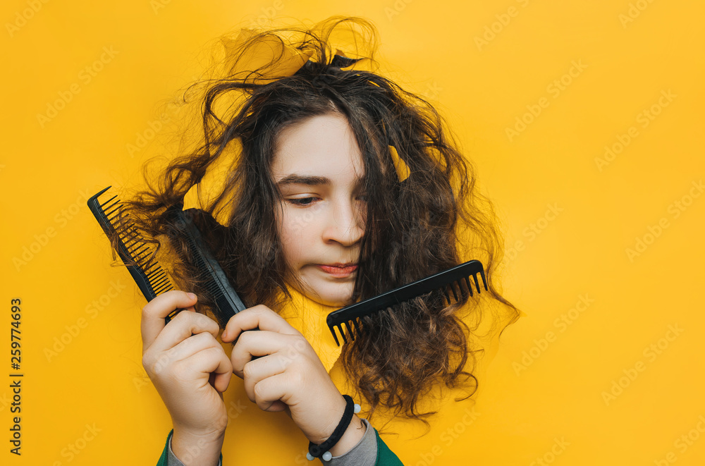 Wall mural A funny teenage sad girl with problematic curly hair expresses displeasure on her face. Three combs tangled in hard hair.