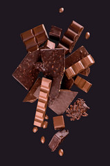 Broken chocolate pieces and cocoa powder on wooden background.