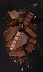 Broken chocolate pieces and cocoa powder on wooden background.