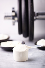 Scoop of Whey Protein, Creatine, Taurine, Beta Alanine capsules and a dumbbell. Bodybuilding food supplements on stone / wooden background. Close up. Copy space.