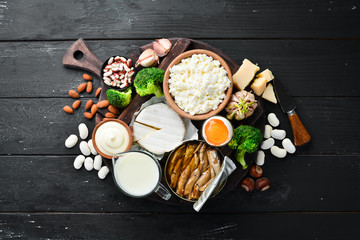 Products containing natural calcium: cheese, milk, parmesan, sour cream, fish, almonds, parsley, garlic, broccoli. On a black wooden background. Top view. Free copy space.