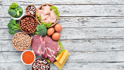 Food high in protein on table. Meat, chicken fillet, broccoli, beans, cheese, eggs, wheat. On a white wooden background.