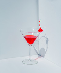 Glass of cocktail and red cherry in a white corner.