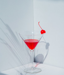 Glass of cocktail and red cherry in a white corner.