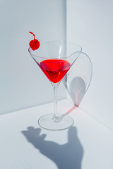 Glass of cocktail and red cherry in a white corner. Natural light 
