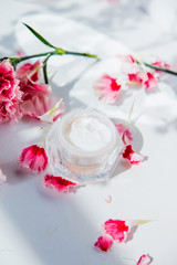 Obraz na płótnie Canvas Skin care cream in boolte and dianthus flowers around on white background