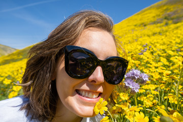 Woman wearing sunglasses sits and poses in a field of yellow wildflowers at Carrizo Plain National...