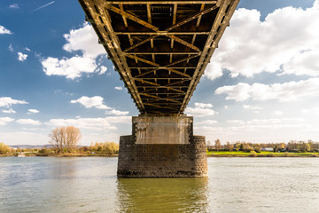 Steel, lattice structure of a railway bridge over a river with a background of blue sky with white clouds in western Germany.