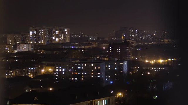 Time lapse of apartment building at night from a window of a skyscaper. Timelapse of residential flats windows lighting up and turning off overnight. Night view of the neighbourhood