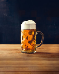 Mug of fresh beer with foam on wooden table