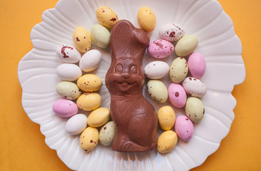 Easter chocolate bunny with colorful eggs on a plate on an orange background.