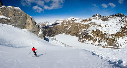 A single skier on Mount Marmolada approaching Fedaia lake, Dolomites, Italy