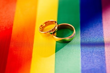 Two gold wedding rings on rainbow lgbt flag. Homosexual marriage.