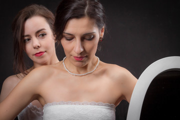 Two young women with vintage hairstyles and bare shoulders stand behind each other on a black background, the foreplay of love. Added a small grain, imitation of film photography