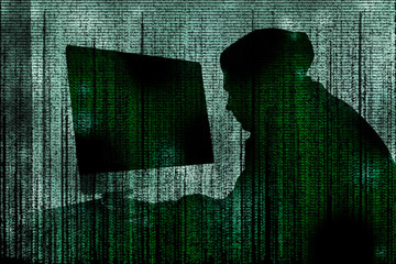 Dark silhouette of cyber criminal hacking computer behind digital symbols