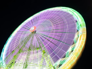 view of a giant ferris wheel attraction in long exposure full of colors at night