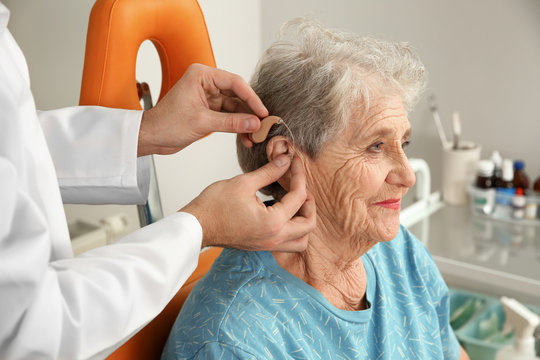 Otolaryngologist putting hearing aid in senior patient's ear at clinic