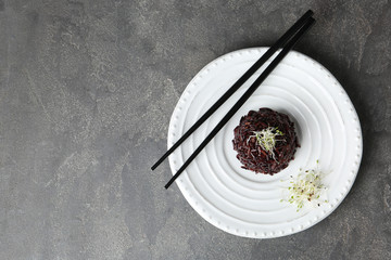 Plate of boiled brown rice and chopsticks on table, top view. Space for text