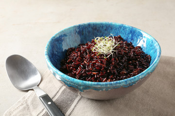 Bowl of boiled brown rice and spoon on table, closeup
