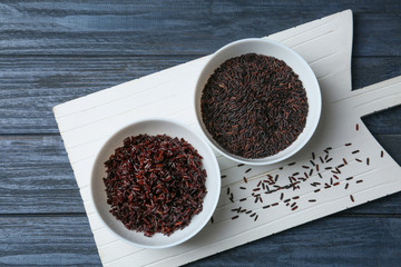 Board with bowls of boiled and uncooked brown rice on table, top view
