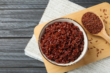 Board with bowl of boiled brown rice and uncooked grains in spoon on table, top view. Space for text