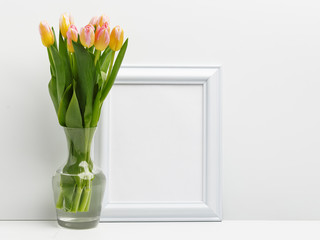 Wooden frame on the table with a bouquet of delicate pink tulips in a glass vase. Copy space.