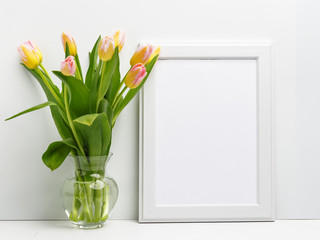 Wooden frame on the table with a bouquet of delicate pink tulips in a glass vase. Copy space.