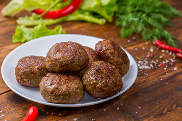 cutlets on a white plate on the background of vegetables and greens. Wooden table and home view