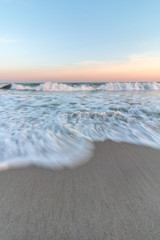 Long exposure of the movement of waves crashing on a sandy beach. Soft orange and blue colors in the sky as the sun sets. 