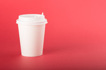 White disposable paper cup with white cap on a red background